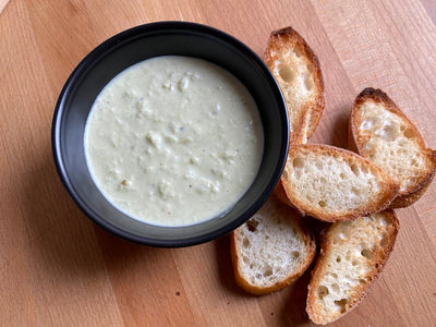 A bowl of lima bean skordalia dip with slices of baguette on a cutting board
