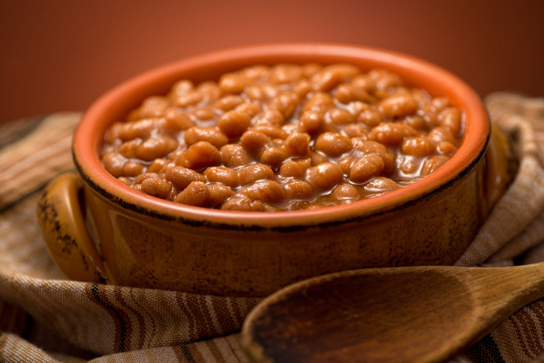 A pot of baked beans swaddled in a towel with a wooden spoon