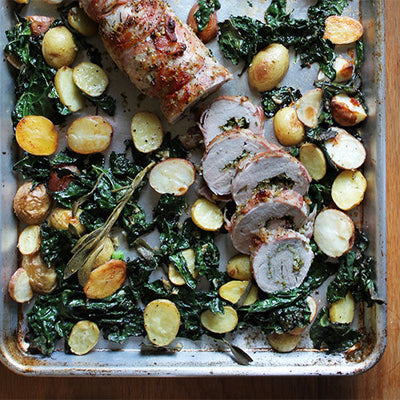 Sliced porchetta with roasted potatoes and kale on a sheet pan