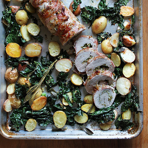 Sliced porchetta with roasted potatoes and kale on a sheet pan