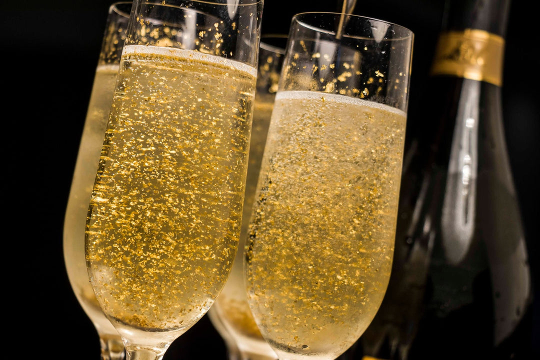 Two champagne flutes filled with sparkling golden champagne, with a dark champagne bottle blurred in the background against a black backdrop.