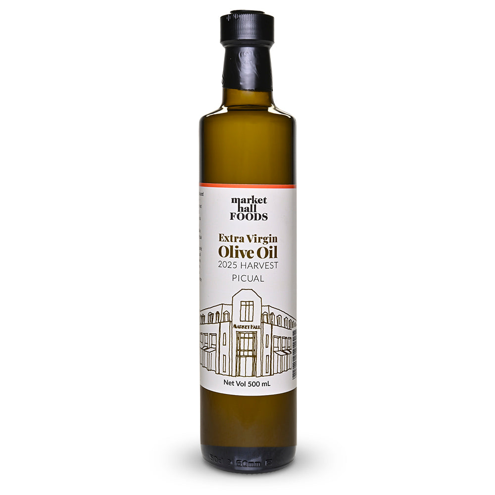 A 500 ml glass bottle of Market Hall Foods Extra Virgin Olive Oil from the 2025 Harvest, featuring a white label with black text and a line drawing of the Picual building, set against a plain white background.