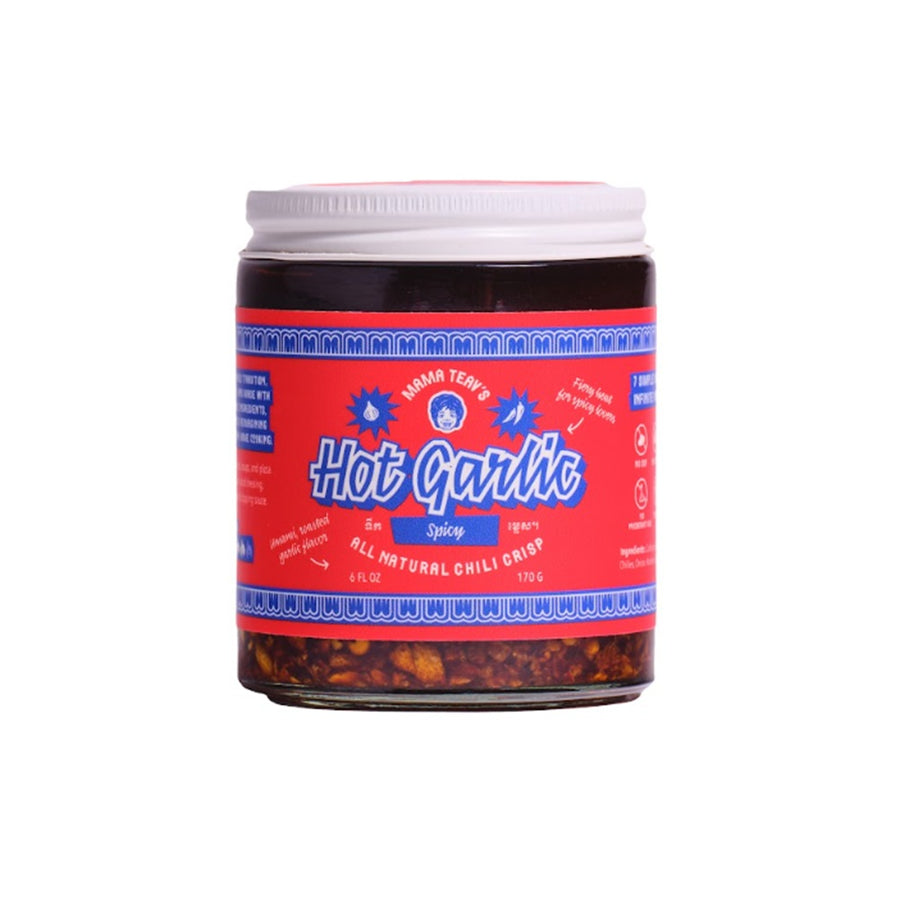 A jar of Mama Teavs Hot Garlic Spicy, featuring a bright red label with blue text and a white lid, set against a plain white background.