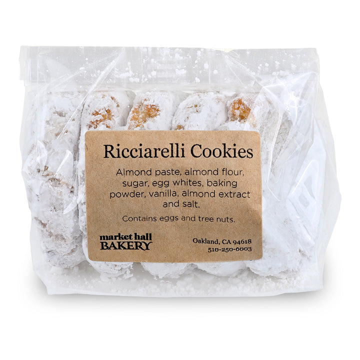 A clear plastic bag of Market Hall Bakery Ricciarelli cookies dusted with powdered sugar, featuring a brown paper label with black text.