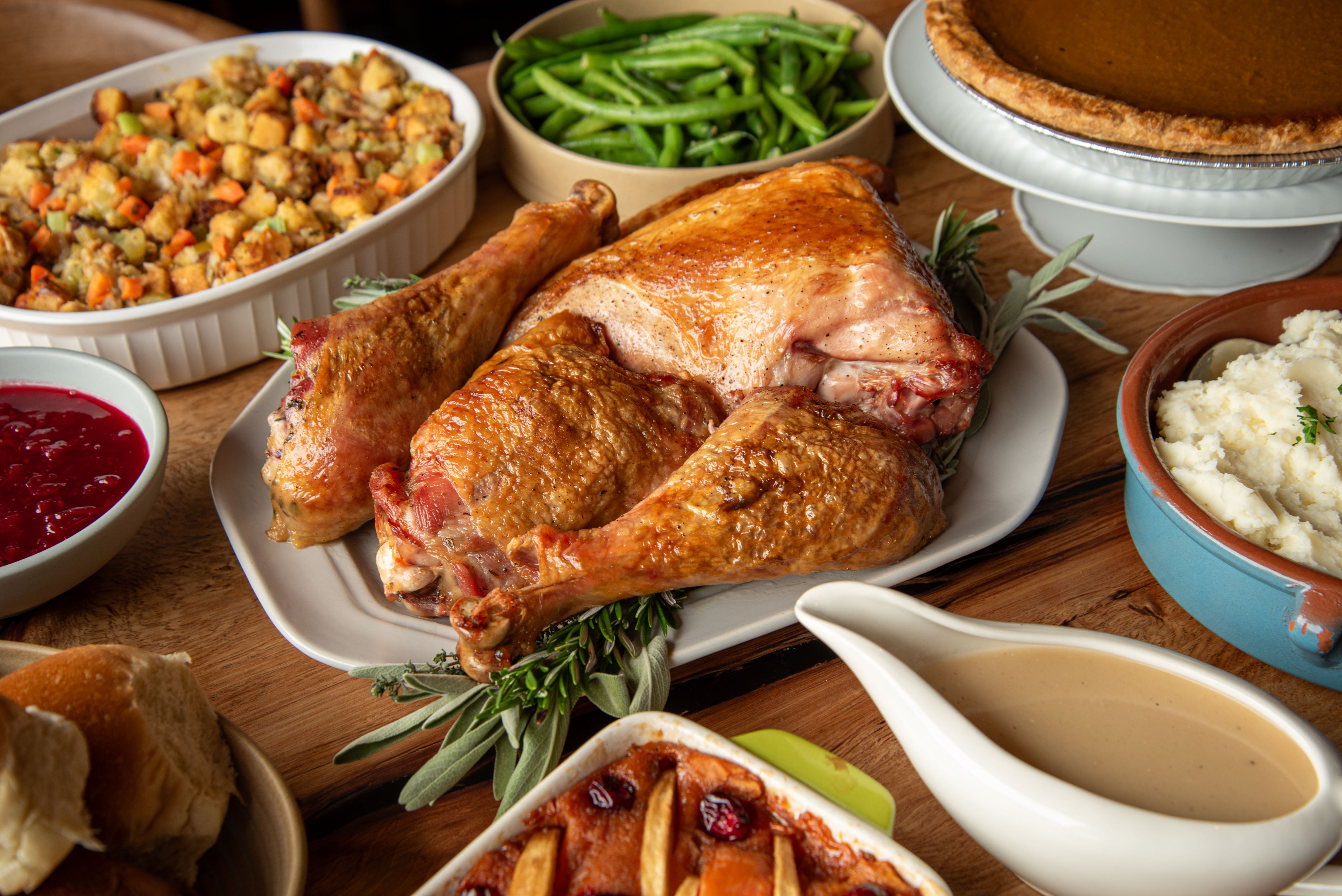 Thanksgiving dinner with roasted turkey, stuffing, green beans, and mashed potatoes on a wooden table.