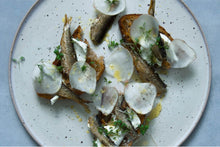 FANGST Nordic Sardines over toast and topped with shaved radish, microgreens and olive oil on a white plate