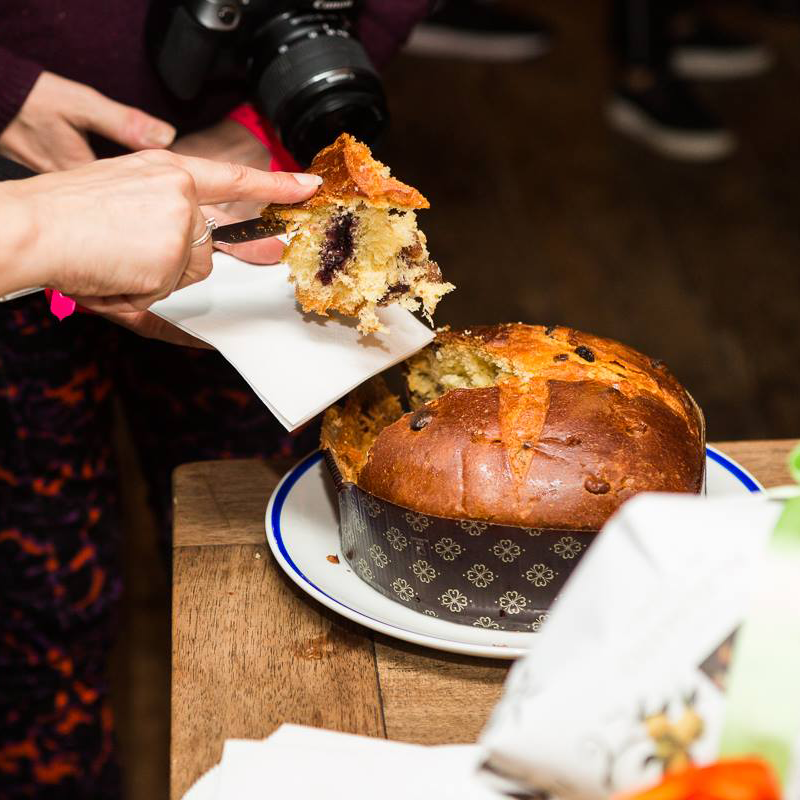 Person holding a piece panettone over a loaf on a wooden table.
