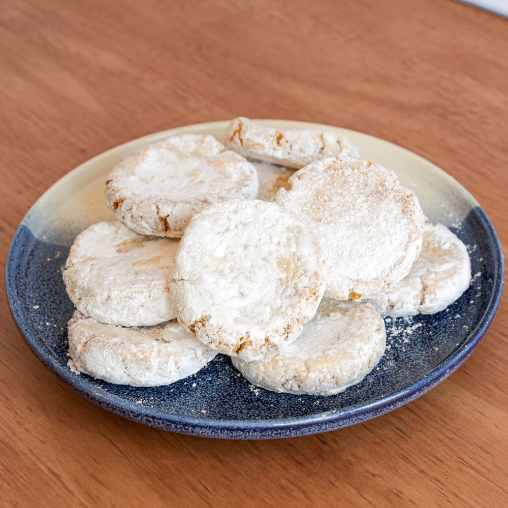 A pile of powdered sugar cookies, served on a speckled blue and beige ceramic plate on a wooden table.