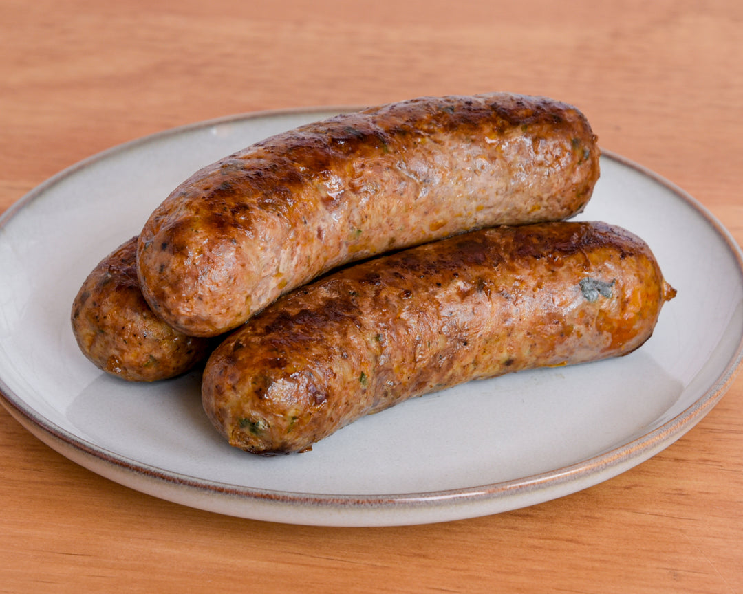 Two cooked sausages on a white ceramic plate with a speckled rim, set on a light brown wooden table.