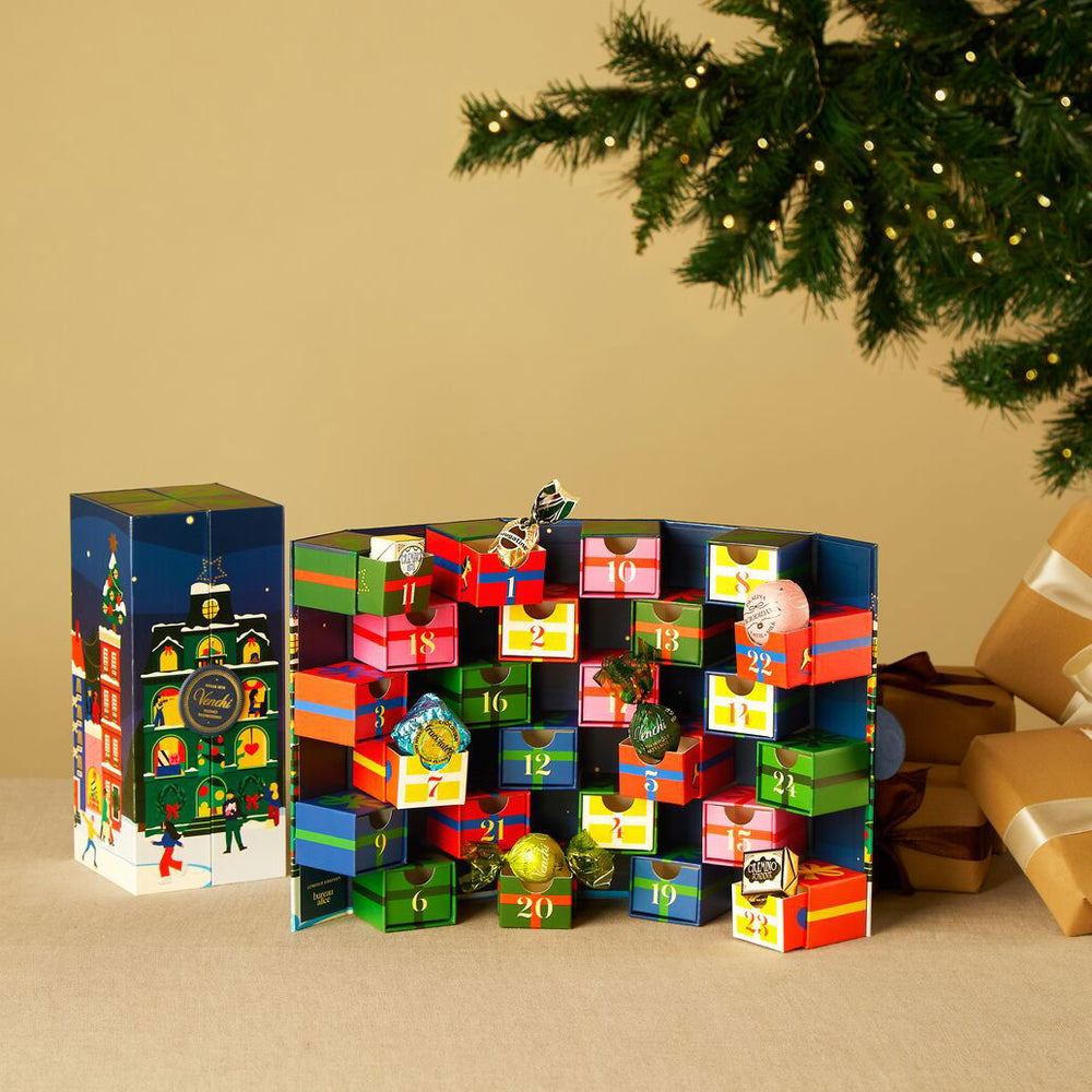 Colorful advent calendar with Christmas decorations on a beige surface with a tree in the background.